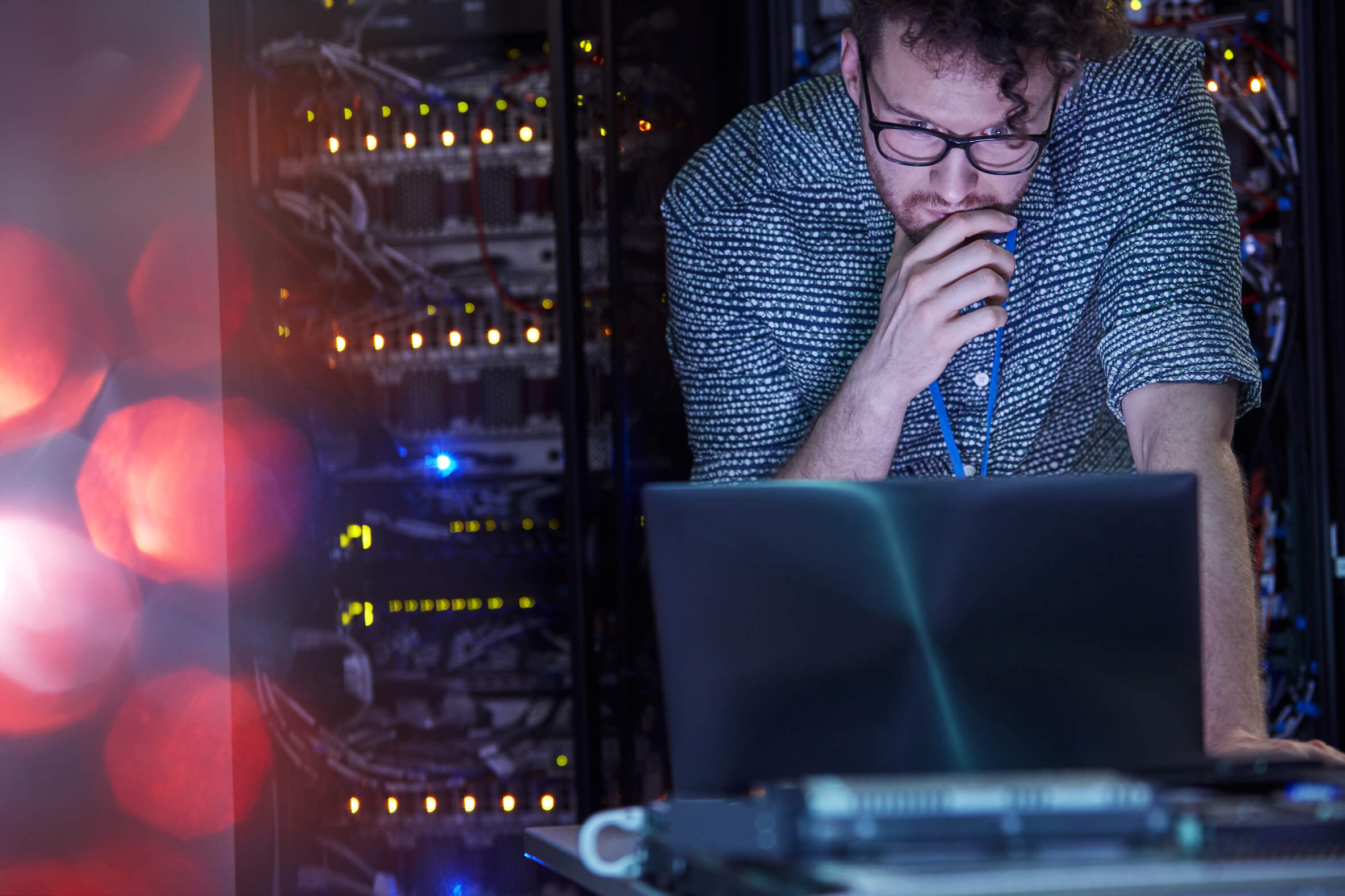En man står i ett serverrum framför en dator och koncentrerar sig på något på en datorskärm.